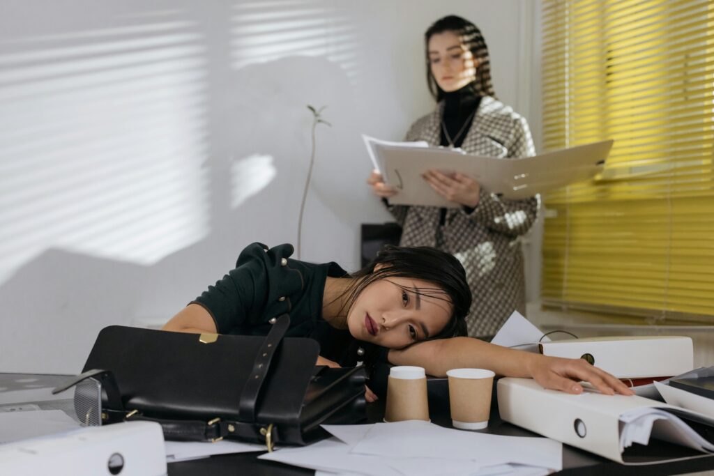 A woman slumped exhausted over her desk surrounded by papers, illustrating founder burnout from servant leadership taken too far