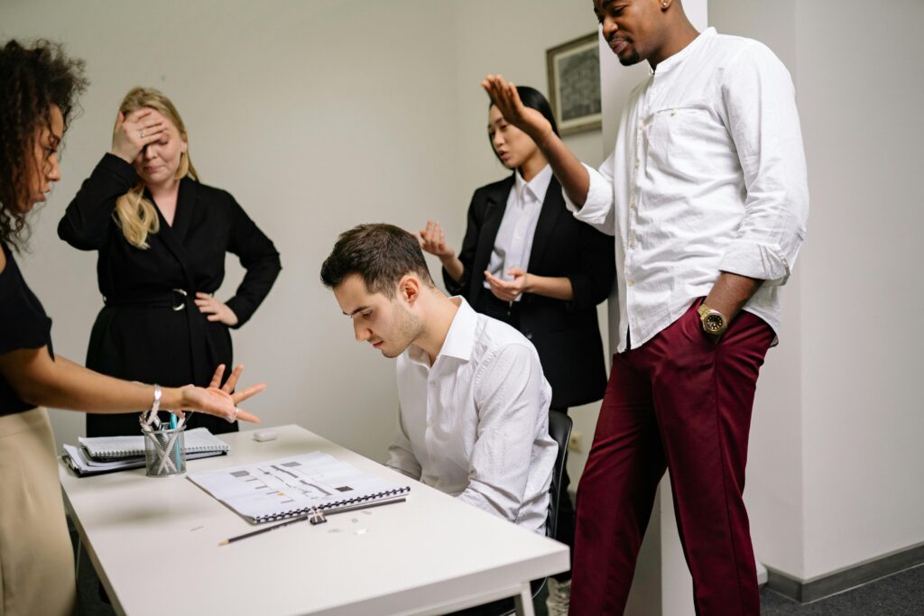 Stressed professional at meeting table surrounded by team members discussing workplace issues