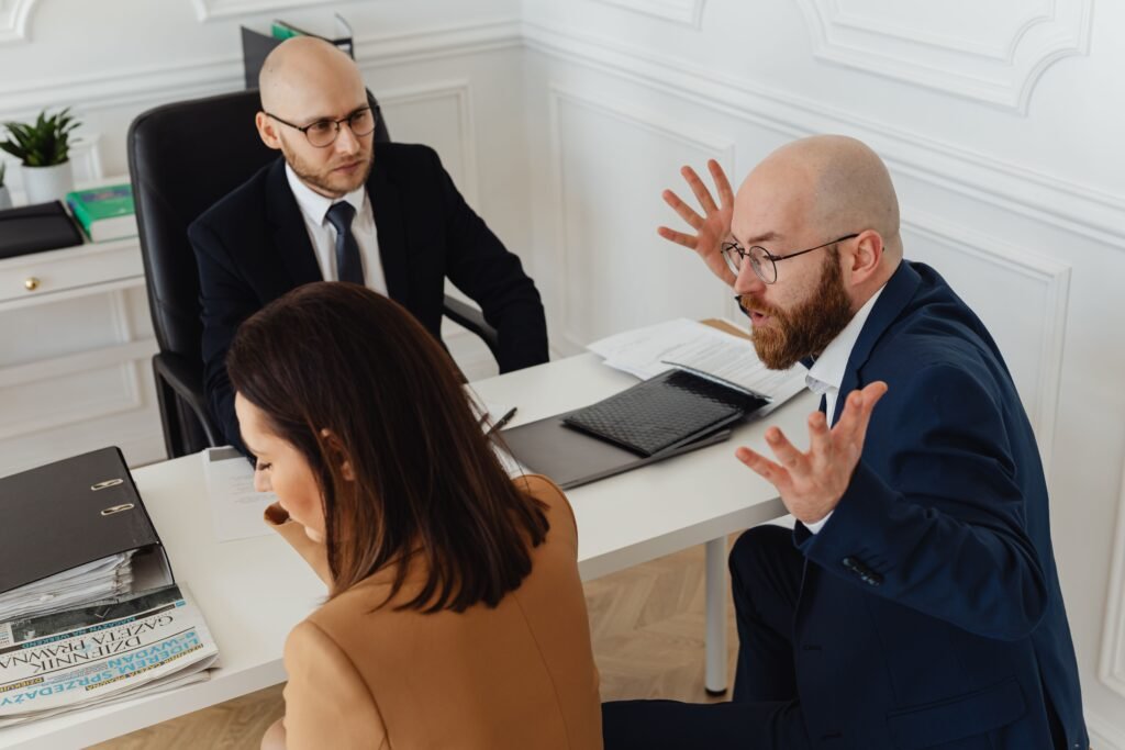Business co-founders in a heated meeting, one gesturing forcefully while others react — depicting a decoy debate